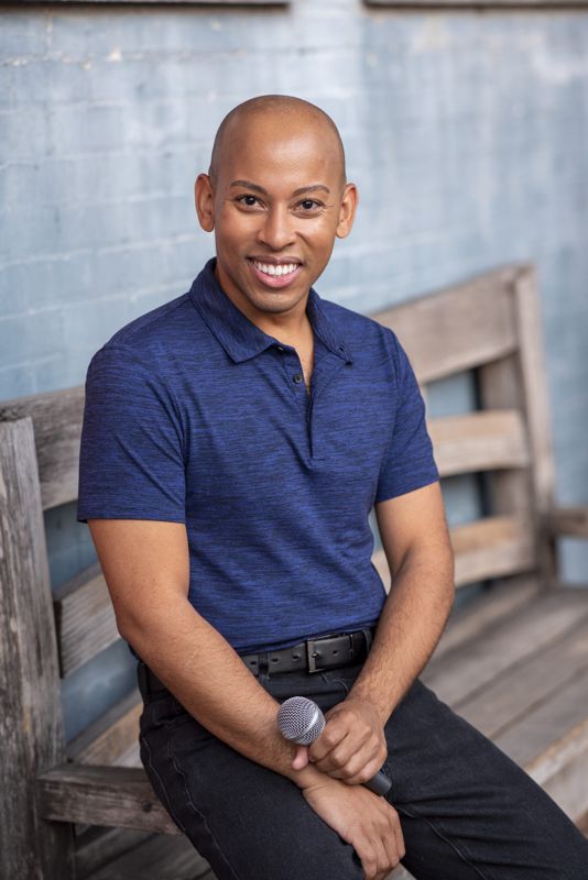 Lemar in a blue polo seated on a bench with a microphone