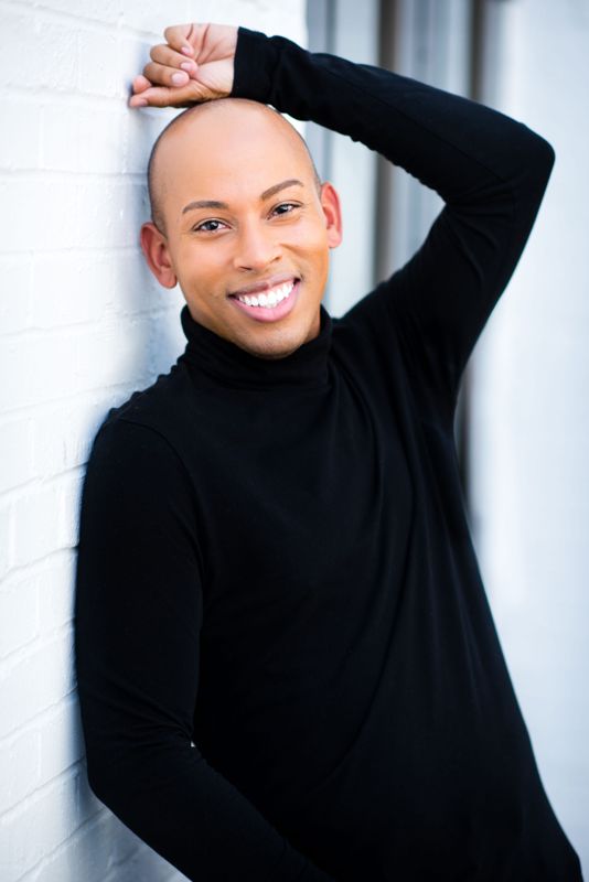 Lemar in a black turtleneck against a white brick wall