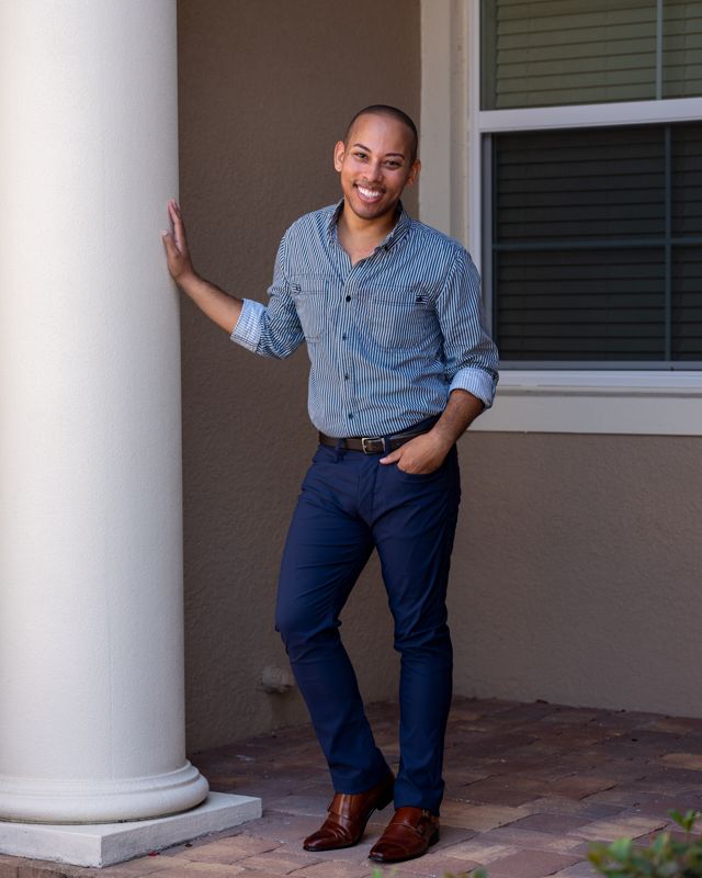 Lemar in a blue shirt leaning on a white column