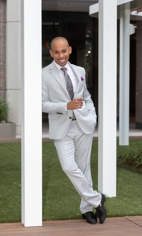 Lemar in a pale grey suit leaning on a white column