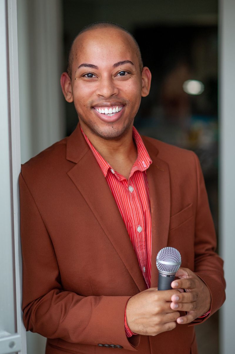 Lemar in a rust jacket holding a microphone, smiling at the audience